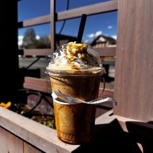 A caramel drink resting on the patio bench under a blue Vernal sky