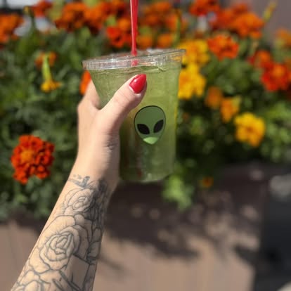 A bright green iced matcha held among orange marigolds